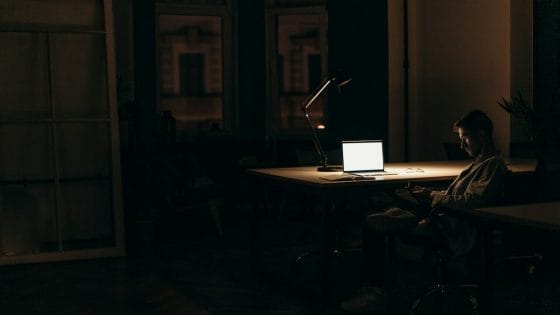 Man sitting in the dark inside a room with a laptop on